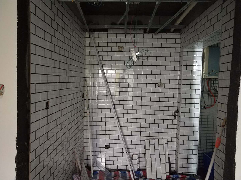 廁所裝修貼瓷磚案例：首先應(yīng)全部清理墻面上的各類污物，打掃干凈現(xiàn)場，特別是腳落里；然后用泥刀先批墻，后用水泥漿找平。這個工序很重要，確保底子平，防止貼后空鼓；以及墻面要刷防水涂料，防止貼后浸水，一般高度不低于1.8米，刷的時候會稍高一些；接著把粘結(jié)劑漿料均勻的刮到墻上，記得瓷磚上墻將經(jīng)過預(yù)先清潔的瓷磚平整地鋪貼在粘結(jié)劑漿料基層上，使用橡膠錘將瓷磚拍實鋪平。施工過程中，可小幅度轉(zhuǎn)動瓷磚，使?jié){料與瓷磚背面充分接觸。