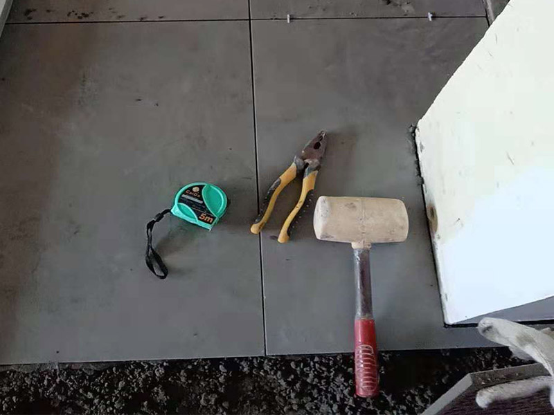 客廳地磚鋪貼：鋪貼的工具包括橡膠錘和粘結(jié)劑。在進行施工之前先把所需要的這些材料都整理好放在一旁備用；基層的處理工作對瓷磚的平整度有很大的影響，對于基層要做好清潔工作，還有找平工作。放樣：在進行瓷磚的鋪貼工作之前還事先找好垂直線，這樣可以在鋪貼的時候找到瓷磚的水平線，讓瓷磚鋪貼的更加的平整。粘結(jié)劑加水攪拌均勻，靜置10分鐘之后就可以使用。將瓷磚表面的浮灰清除，再在瓷磚背面均勻的涂抹上粘結(jié)劑，按照預鋪的順序?qū)⒋纱u鋪貼在地面上，最后用橡膠錘輕輕拍打至服帖齊整。