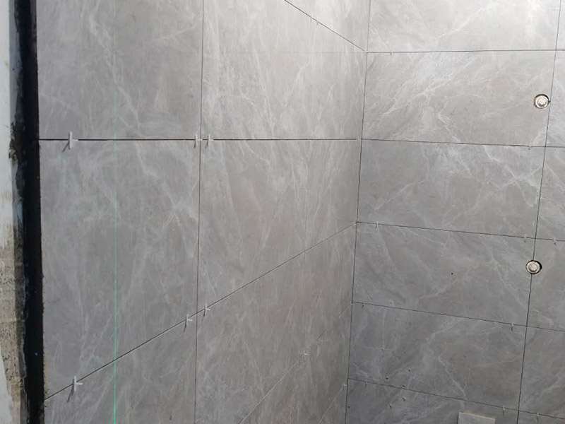 衛(wèi)生間貼磚施工：應(yīng)全部清理墻面上的各類污物，打掃干凈現(xiàn)場(chǎng)，特別是腳落里。用泥刀先批墻，后用水泥漿找平。這個(gè)工序很重要，確保底子平，防止貼后空鼓。墻面要刷防水涂料，防止貼后浸水，一般高度不低于1.8米，刷的時(shí)候會(huì)稍高一些。根據(jù)設(shè)計(jì)鋪貼圖樣的要求，確定排磚方案，用墨斗彈線，以減少施工損耗。把剛剛攪拌好的粘結(jié)劑漿料均勻的刮到墻上。瓷磚上墻將經(jīng)過預(yù)先清潔的瓷磚平整地鋪貼在粘結(jié)劑漿料基層上，使用橡膠錘將瓷磚拍實(shí)鋪平。施工過程中，可小幅度轉(zhuǎn)動(dòng)瓷磚，使?jié){料與瓷磚背面充分接觸。專家建議在鋪貼時(shí)，隨機(jī)取下已鋪貼于基層上的瓷磚作檢查。確保漿料與瓷磚背面的充分接觸。 留縫大小調(diào)整根據(jù)瓷磚的尺寸，在磚與磚之間預(yù)留相應(yīng)尺寸的縫隙留待嵌縫?？捎醚篮灥认裙潭ǎ辰Y(jié)劑具有一定的可調(diào)整性，可對(duì)留縫的大小進(jìn)行調(diào)整。