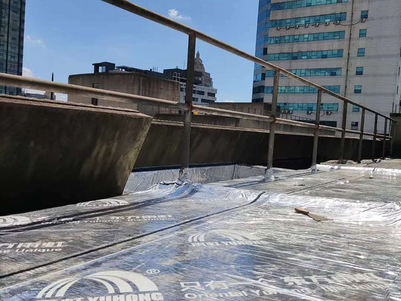 屋頂防水卷材鋪貼:1、由于設(shè)計要求屋面找坡層按2％坡度放坡，因此卷材鋪設(shè)時應(yīng)平行于屋脊自下而上的鋪貼，卷材搭縫必須嚴(yán)密，縫口應(yīng)順?biāo)鞣较虼罱?，其寬度不?yīng)小于50mm，上下屋接縫應(yīng)左右錯開250mm，在鋪大面積防水卷材之前，應(yīng)將檐溝，管道口、雨水口處的附加防水布鋪好后由屋頂?shù)牡吞幭蚋咛庍M行大面積的鋪貼。 2、屋頂卷材遇到女兒墻時，應(yīng)將卷材沿墻上卷，高度應(yīng)低于250mm，然后固定在墻上預(yù)埋的木磚和木塊上，并用1：3水泥砂漿做坡水。 3、凡管道等伸出屋面的構(gòu)件必須在屋頂上開孔時，為了防漏水應(yīng)將卷材向上翻起，抹以水泥砂漿或再蓋上鍍鋅鐵皮起擋水作用，泛水高度不超過200mm。 防水材料卷材層應(yīng)粘結(jié)牢固，無空鼓、損傷、滑移，翹邊、起泡、皺折等缺陷。防水工程施工完畢后，必須作蓄水試驗合格后開始進行下道工序。